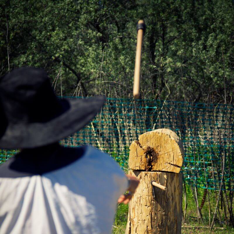 an outdoor photo of a person with a black hat throwing an axe at a tree stump