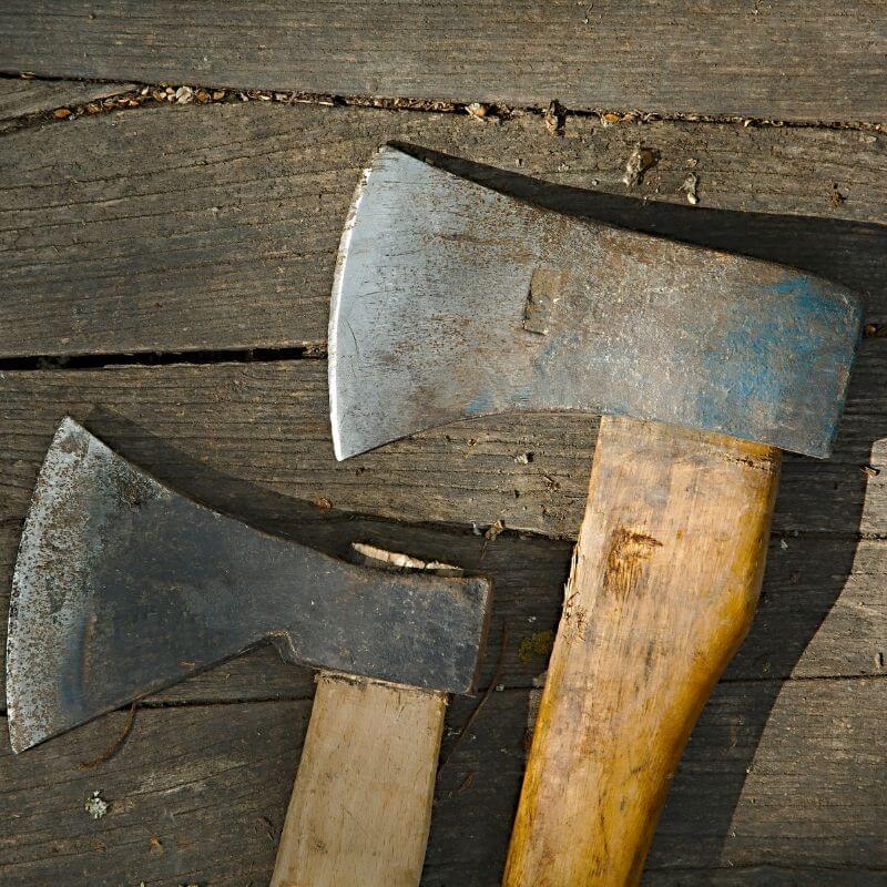 close up of two dirty axes on a wooden floor outside
